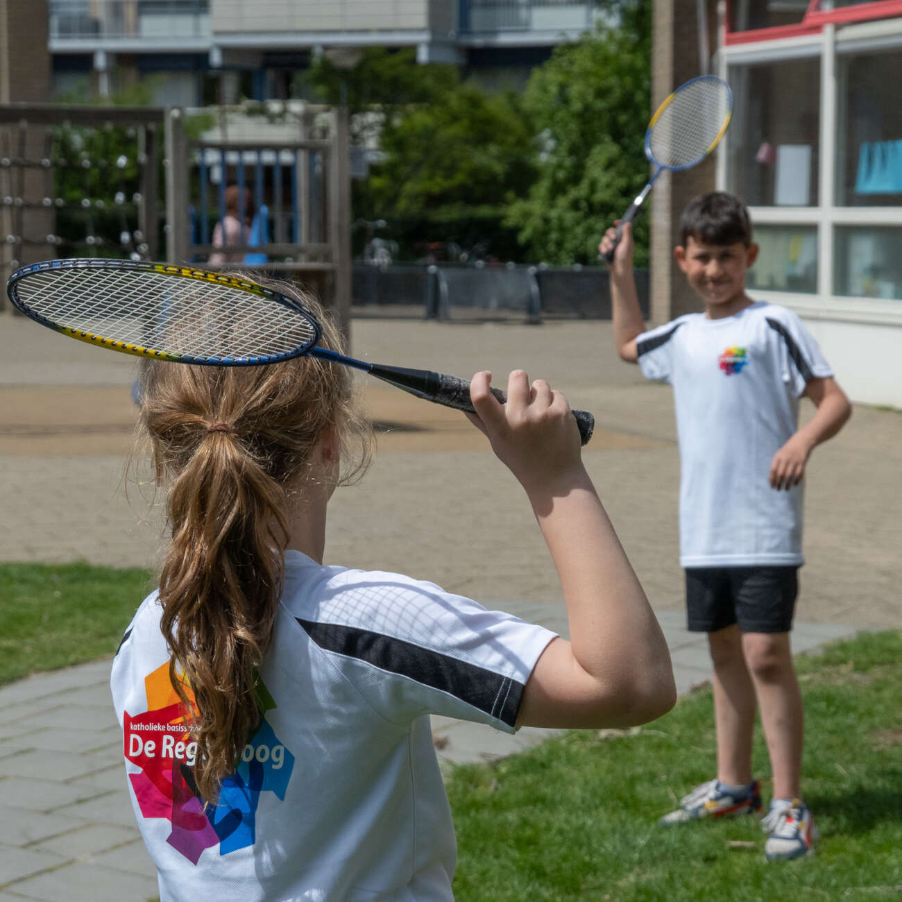 Twee leerlingen van De Regenboog spelen badminton op het schoolplein
